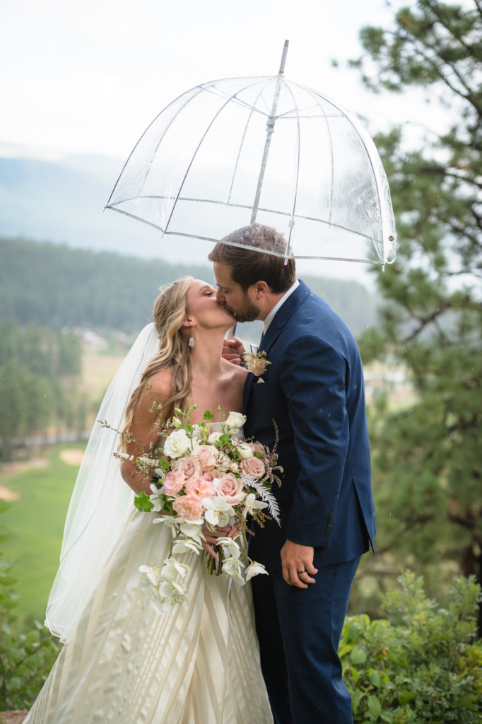 bride and groom under umbrella rainy ceremony at glacier club wedding picture