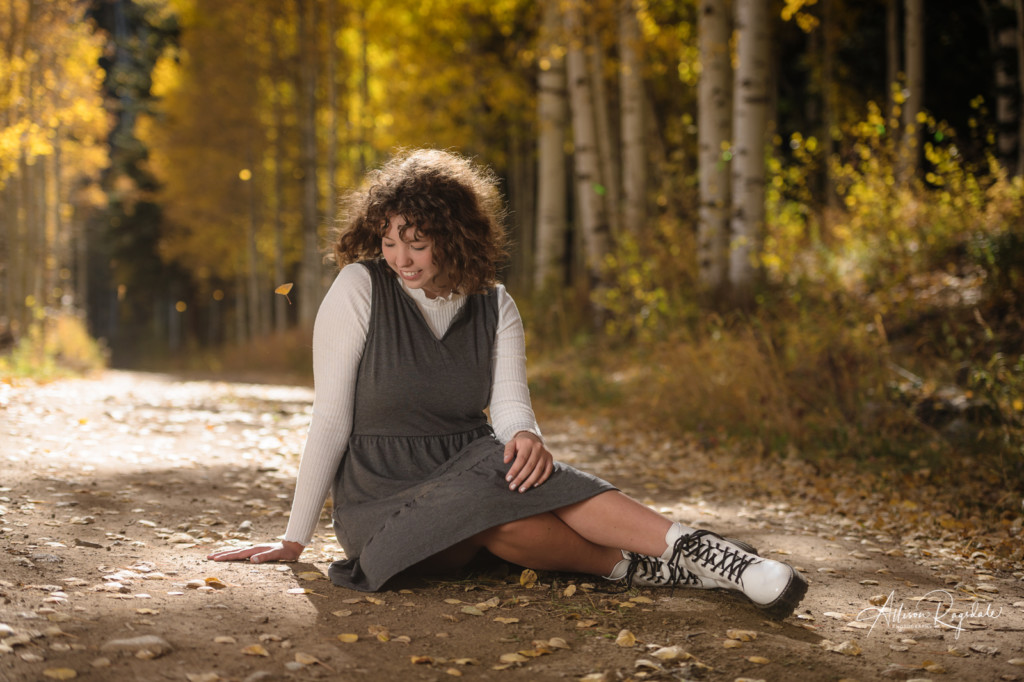 senior picture girl sitting on dirt road with aspen leaves falling around her