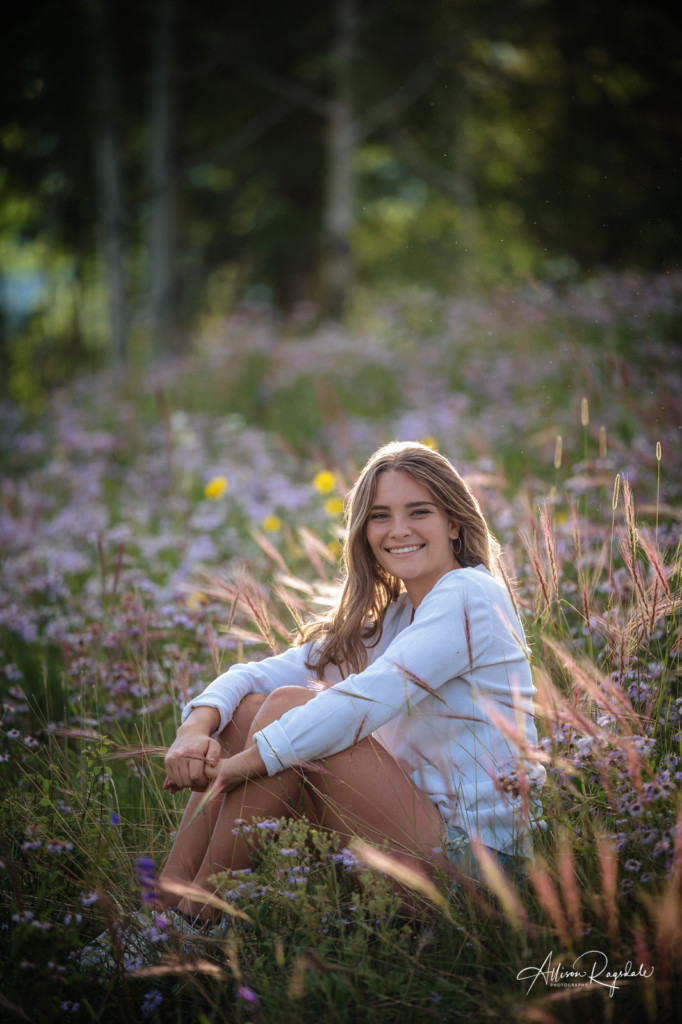 girl senior photo sitting in long grass and wildflowers