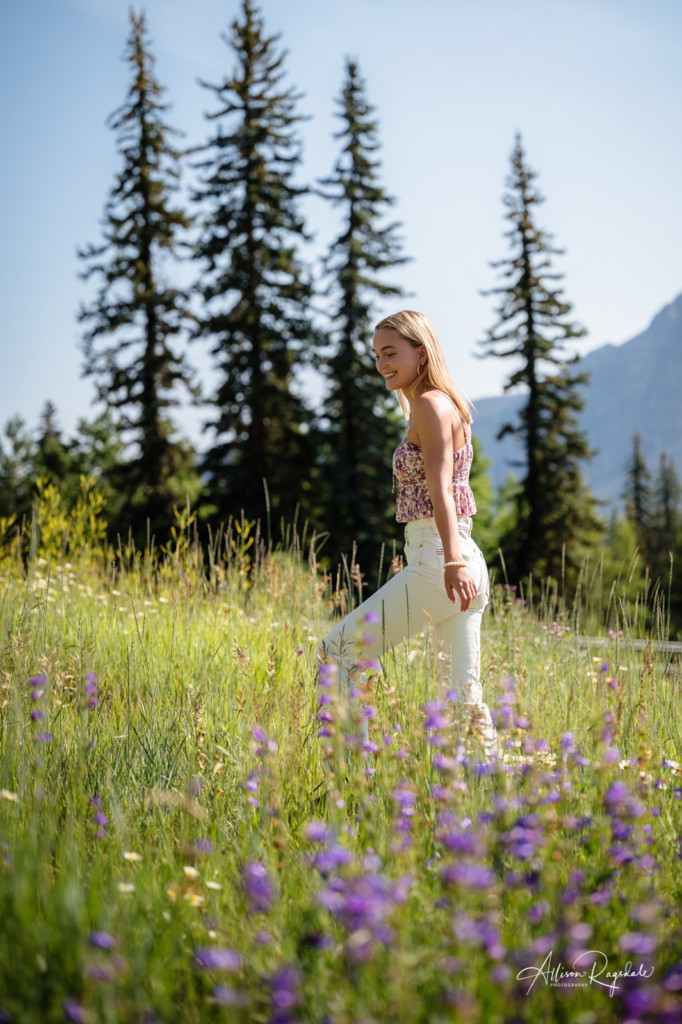 walking through wildflowers with pine tree background senior girl photo