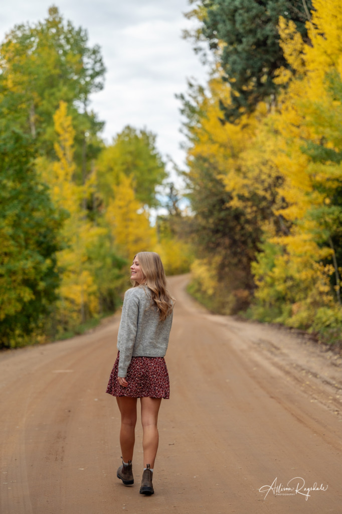 girl walking away dirt road lined with fall colors senior photo