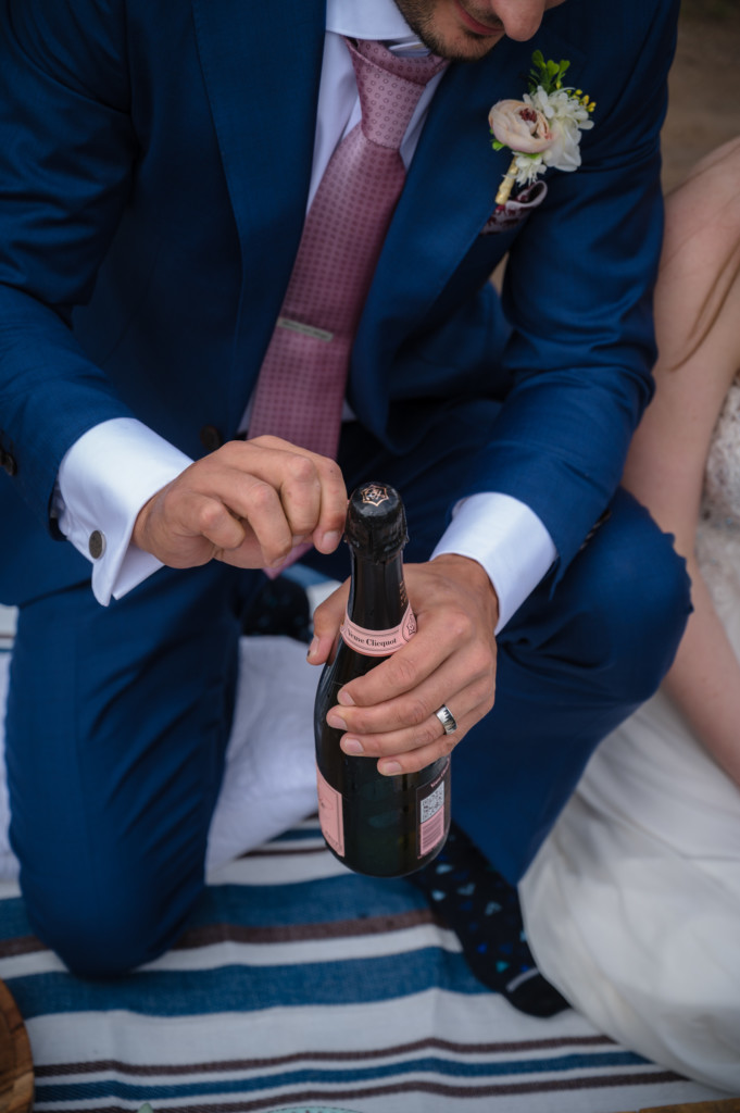 groom opening champagne bottle elopement picnic photo