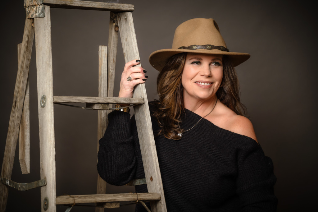 studio portrait cowgirl hat off the shoulder black sweater with rustic ladder